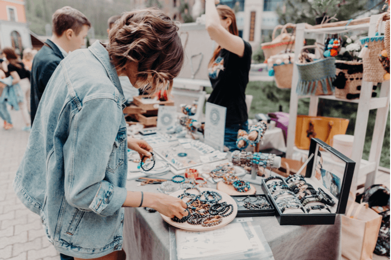 Person browsing jewlery at craft market.